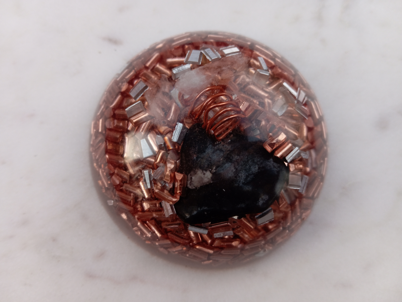 Shungite, connue pour absorber les ondes nocives
* Cristal de roche, entouré de fil de cuivre, pour canaliser les énergies
* Copeaux d’aluminium et de cuivre, pour équilibrer le champ ambiant
* Résine epoxy, pour un rendu esthétique